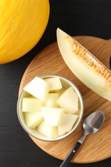 Cut and whole ripe melons on black wooden table, flat lay