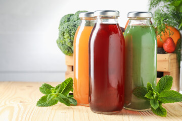 Tasty juices in glass bottles, fresh ingredients and herbs on wooden table against light grey background, closeup