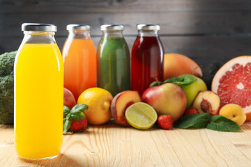 Tasty juices in glass bottles, fresh ingredients and herbs on wooden table against brown...