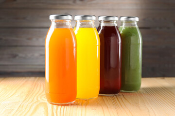 Tasty juices in glass bottles on wooden table against brown background, closeup