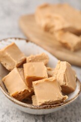 Homemade caramel candies in bowl on light grey table, closeup