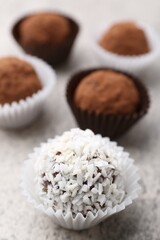 Delicious homemade candies with cocoa powder and coconut flakes on light grey table, closeup