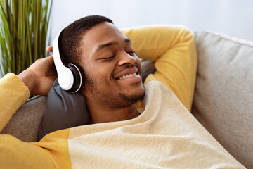 Closeup of relaxed black guy listening to music, using headset, copy space. Happy african american...