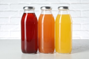 Tasty juices in glass bottles on white table against brick wall
