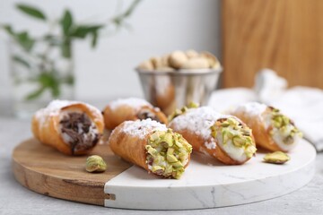 Delicious cannoli with ricotta cheese, pistachios, chocolate and powdered sugar on light grey table indoors, closeup
