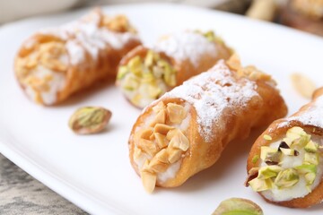 Delicious cannoli with ricotta cheese, peanuts, pistachios and powdered sugar on grey textured table, closeup
