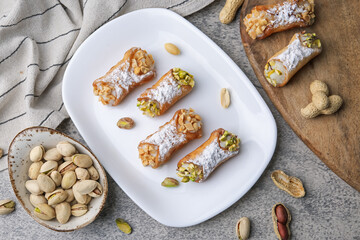 Delicious cannoli with ricotta cheese, peanuts, pistachios and powdered sugar on grey textured...