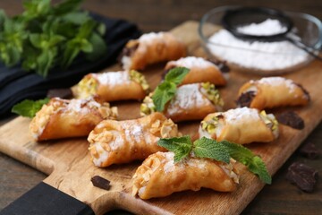 Delicious cannoli with cheese, nuts, chocolate, mint and powdered sugar on wooden table, closeup