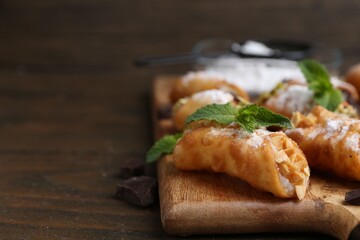 Delicious cannoli with cheese, nuts, chocolate, mint and powdered sugar on wooden table, closeup. Space for text