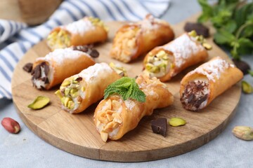 Delicious cannoli with cheese, nuts, powdered sugar, chocolate and mint on grey table, closeup