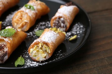 Delicious cannoli with cheese, nuts, powdered sugar, chocolate and mint on wooden table, closeup