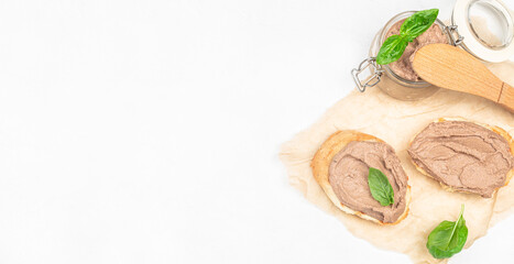Toasted bread with creamy liver pate and fresh basil leaves on parchment. Long banner format. top view. copy space