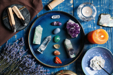 Chakra gemstones, lavender flowers, incense, palo santo and burning candles on blue wooden table,...