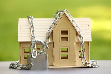 Home security. House model, chain and padlock on light table outdoors, closeup