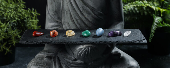 Statue with chakra gemstones and plants on black table, closeup