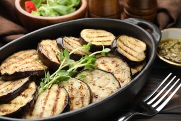 Grilled slices of eggplant with microgreens served on wooden table, closeup