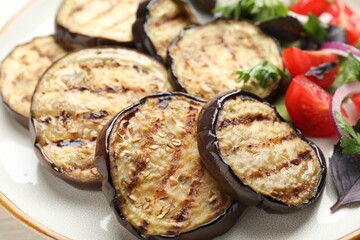 Grilled slices of eggplant with salad on white table, closeup