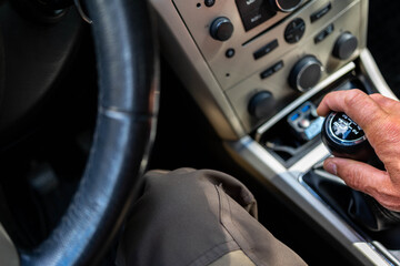 Caucasian man driving, shifting gears on manual gearbox, focus on the mans hand.