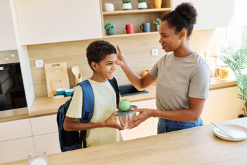 Mother helping son to get ready for school, helping him with backpack and books, and making snack...