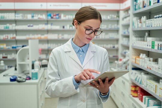 Pharmacist using tablet in pharmacy with shelves filled with medicine and medical supplies behind her
