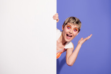 Cheerful young woman peeking around a white panel in a vibrant retro style against a purple...