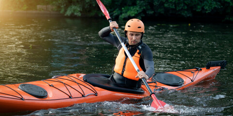 Man in a helmet and life jacket paddles an orange kayak on a calm river. Training in rowing skills and water stability