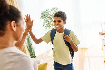 Mother helping son to get ready for school, helping him with backpack and books, high five and...