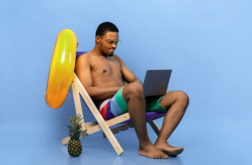 Computer problems. Frustrated black guy having trouble with laptop while sitting in lounge chair on...