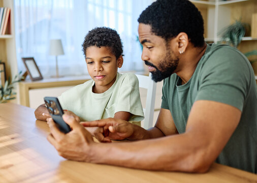 Teenage boy with his father and using phone and doing homework. Father and son bonding and having fun at home