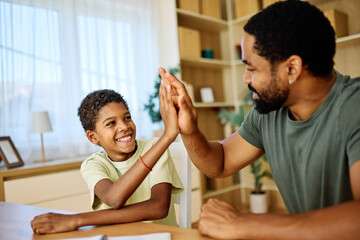 Father and son doing homework  at home.  Father and son giving high five hand to each other....