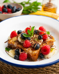 French toast cooked with butter and with red fruits and banana.