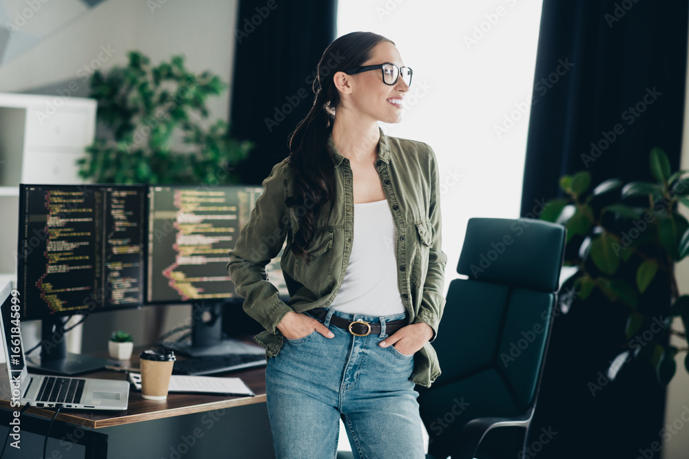 Poster confident female it specialist standing in a modern office workspace surrounded by computer monitors