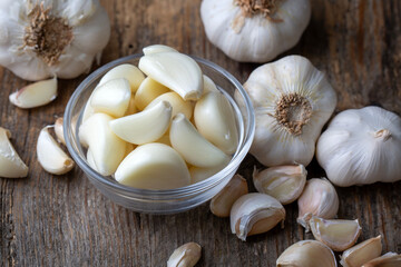 Garlic cloves in a glass bowl with peeled garlic on a white wooden table.