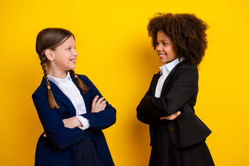 Two smiling young schoolgirls standing on a yellow background, embracing diversity and friendship while wearing formal school uniforms