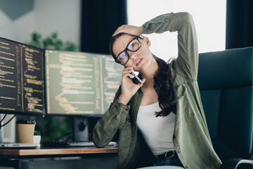 Professional woman working remotely on computer programming tasks in a modern office setting with dual monitors.