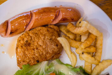 Pork steak and hot dog served with french fries. Close up