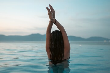 beautiful woman swimming in luxury pool at sunset flowing into sea, elegant vacation and tropical serenity, stunning girl relaxing in lavish resort pool at sunrise