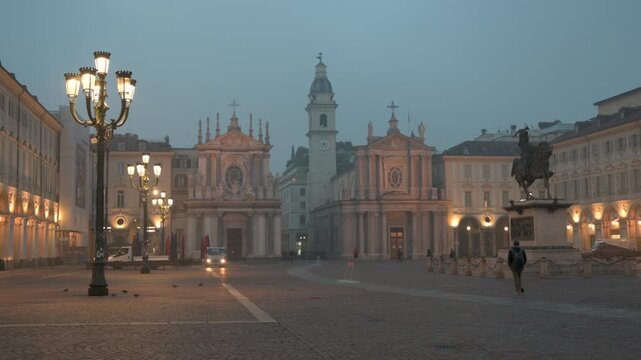 Turin, Piedmont, Italy. November 20, 2024. Early morning in Piazza San Carlo, a city icon. The two twin churches that characterize the square stand out. Passersby. On the left, a streetlight is lit.
