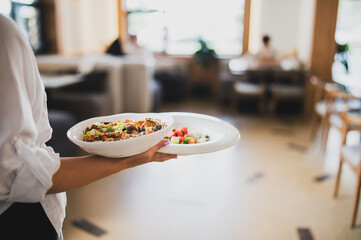 Waiter in white shirt serving two plates with gourmet food and fresh salad in a bright, modern...
