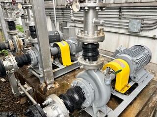 A series of large industrial pumps with electric motors are connected to a network of pipes in a factory setting, all coated in a dull gray finish.