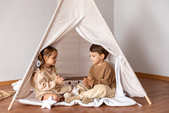Happy little children siblings boy and girl sitting in a wigwam tent, playing and having fun at home. Children's room, childhood, games, imagination. High quality photo - Powered by Adobe