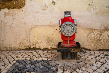 Red fire hydrant in front of old textured wall and cobblestone pavement, urban safety...