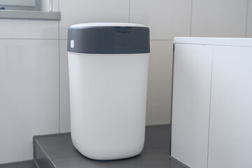 modern diaper disposal bin with a sleek design placed beside a white cabinet, showcasing functionality and cleanliness in a bright bathroom setting