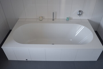 Fototapeta premium elegantly designed white oval bathtub positioned against a seamless white tiled wall, featuring modern chrome fixtures and accompanied by minimalist decorative candles for a serene bathroom ambiance