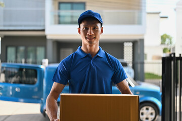 Portrait of a Friendly deliveryman holding a cardboard box while standing at the customer's front door