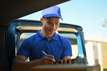 An Asian Deliveryman in uniform using a stylus on a digital tablet to check and record packages during delivery