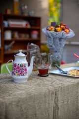 Outdoor table with tea pot, juice jug, pastries and bouquet of flowers.