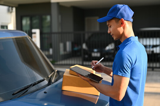 Deliveryman in blue uniform records parcel information on a tablet placed on the vehicle hood