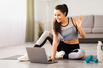 Smiling beautiful lady in sportswear having online conference with fitness trainer from home,...