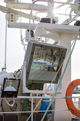A mast of a boat, featuring large deck floodlights and a marine radar scanner. The floodlights are used for illuminating the deck during nighttime, the radar for navigation and collision avoidance.